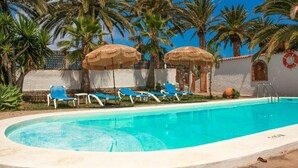 A pool area with blue lounge chairs and thatched umbrellas, surrounded by palm trees. - Finca El Castillo (Buenavista del Norte)