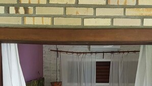 Un lit simple avec une couverture à rayures, une petite table sur laquelle est posé un vase, et une fenêtre avec des rideaux.