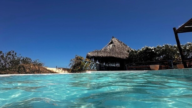 Une piscine d’eau turquoise aux eaux limpides, avec une structure à toit de chaume en arrière-plan.
