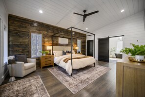 A modern bedroom with a wooden accent wall, a canopy bed, and a ceiling fan. - Romantic,Spacious,Modern Cabin | Hot Tub! (Broken Bow)