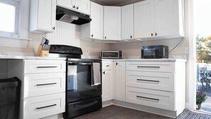 Une cuisine avec des meubles blancs, un four noir, un four à micro-ondes et un grille-pain.