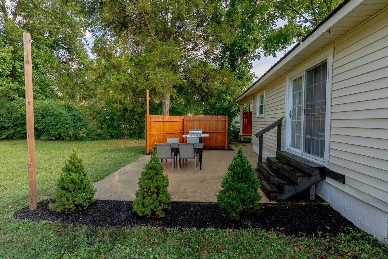 Un patio trasero residencial con un porche, cerco de madera y una casa.