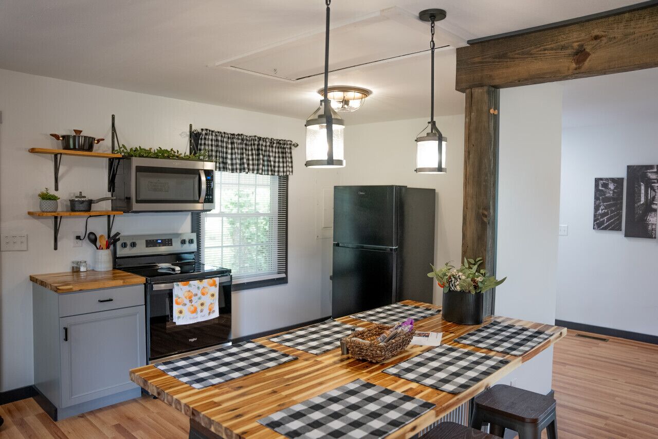 Une cuisine moderne avec une table en bois, des tapis à carreaux, un four à micro-ondes, un four, un réfrigérateur et des luminaires suspendus.