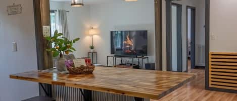 Un comedor moderno con una mesa de madera, taburetes de bar, un televisor y una chimenea.