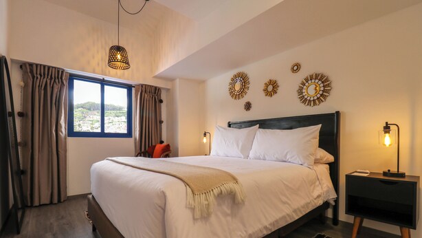 Un dormitorio con una cama grande, una ventana con cortinas, detalles decorativos en la pared y lámparas de noche.