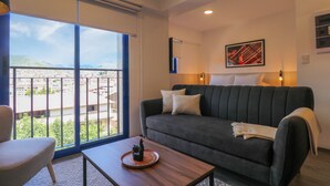 Una sala de estar moderna con un sofá, una mesa de centro y vistas a un paisaje urbano a través de grandes ventanales.
