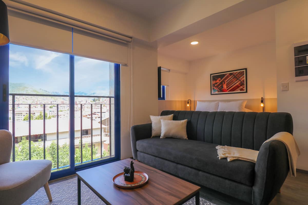 Una sala de estar moderna con un sofá, una mesa de centro y vistas a un paisaje urbano a través de grandes ventanales.