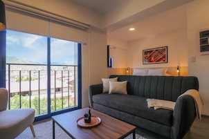 Una sala de estar moderna con un sofá, una mesa de centro y vistas a un paisaje urbano a través de grandes ventanales.