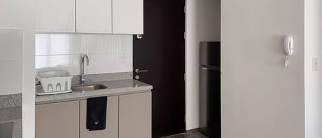 A modern kitchen with a granite countertop, white cabinets, a black refrigerator, and a built-in phone.
