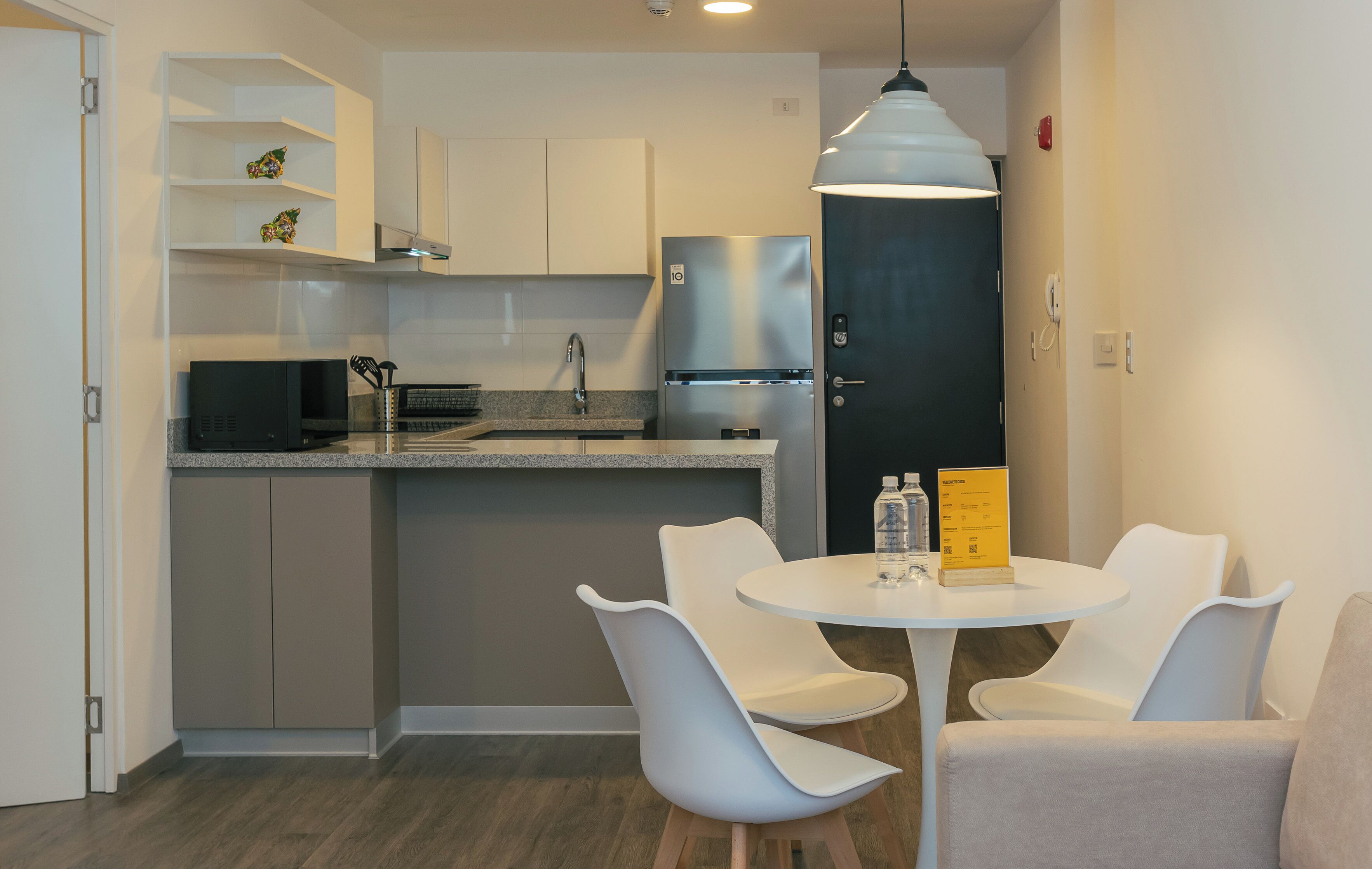 A modern kitchen with white cabinets, a stainless steel refrigerator, and a dining area with a round table and two chairs.