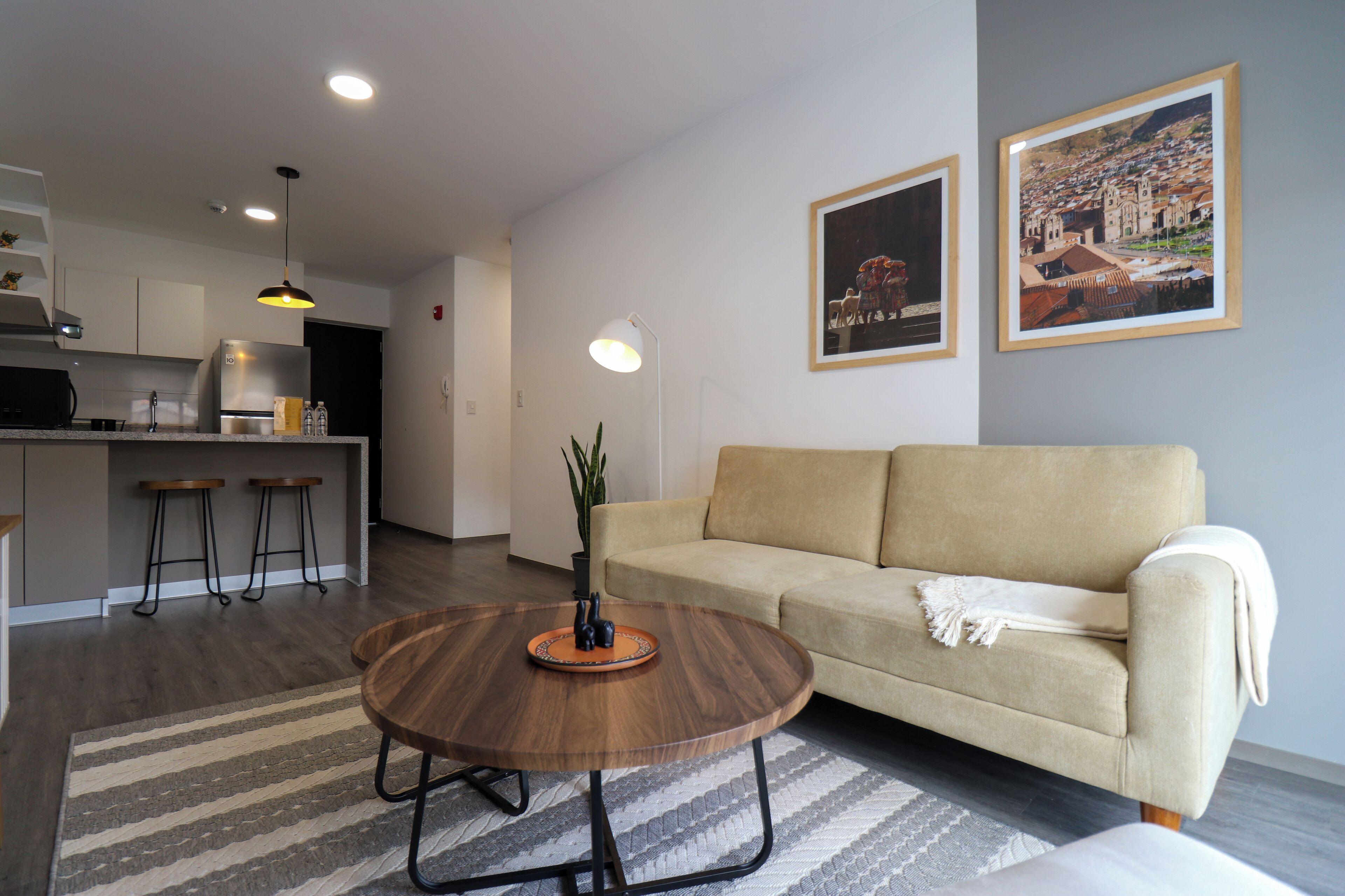 A modern living room with a sofa, a round wooden coffee table, and a kitchen in the background.