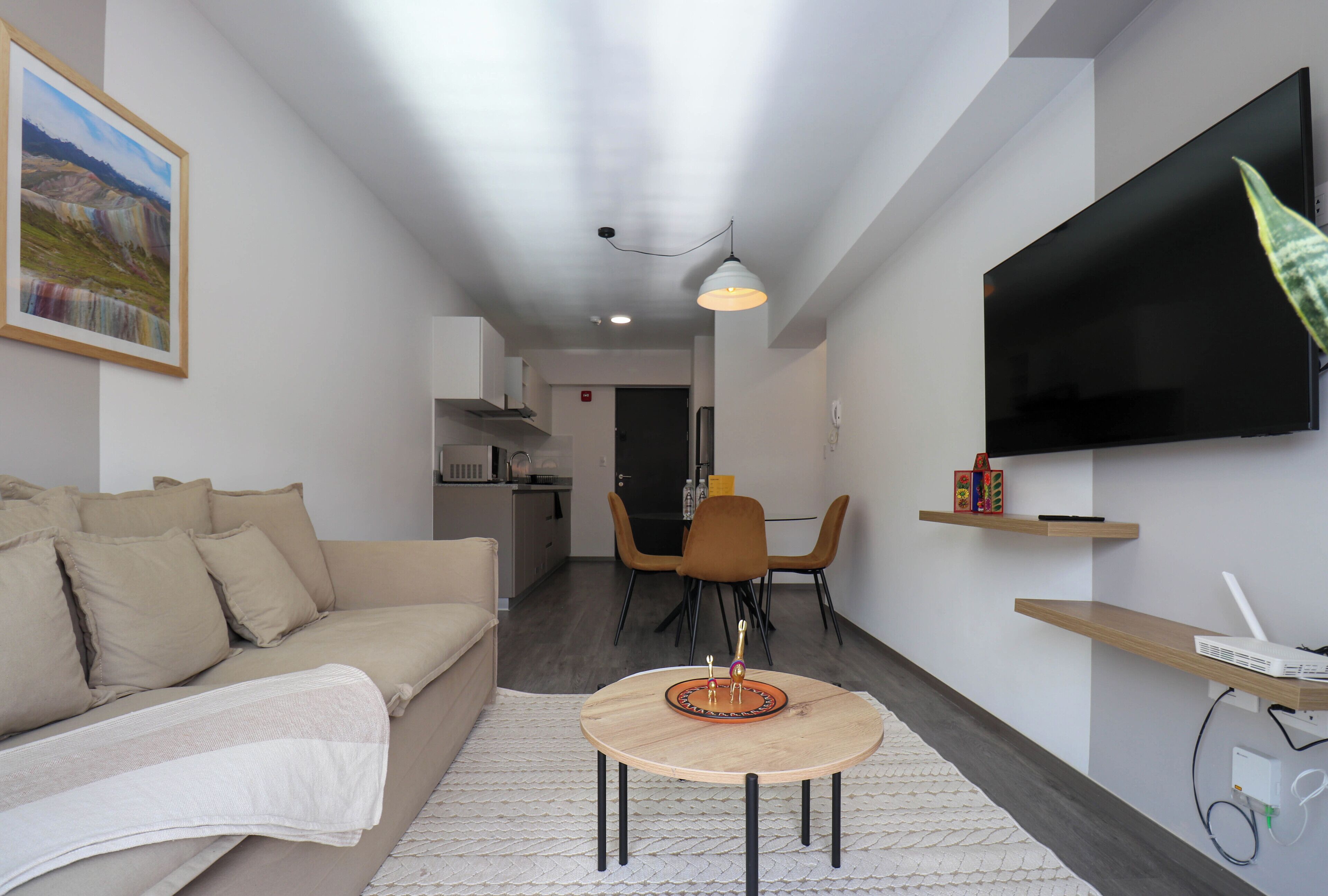 A modern living room with a sofa, a round table, a TV, and a dining area with chairs.