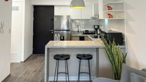 Una cocina moderna con una isla central, taburetes de bar, un refrigerador y una lámpara colgante.