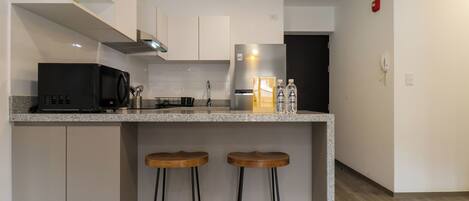 A modern kitchen with a built-in island, bar stools, a microwave, a refrigerator, and a pendant light.