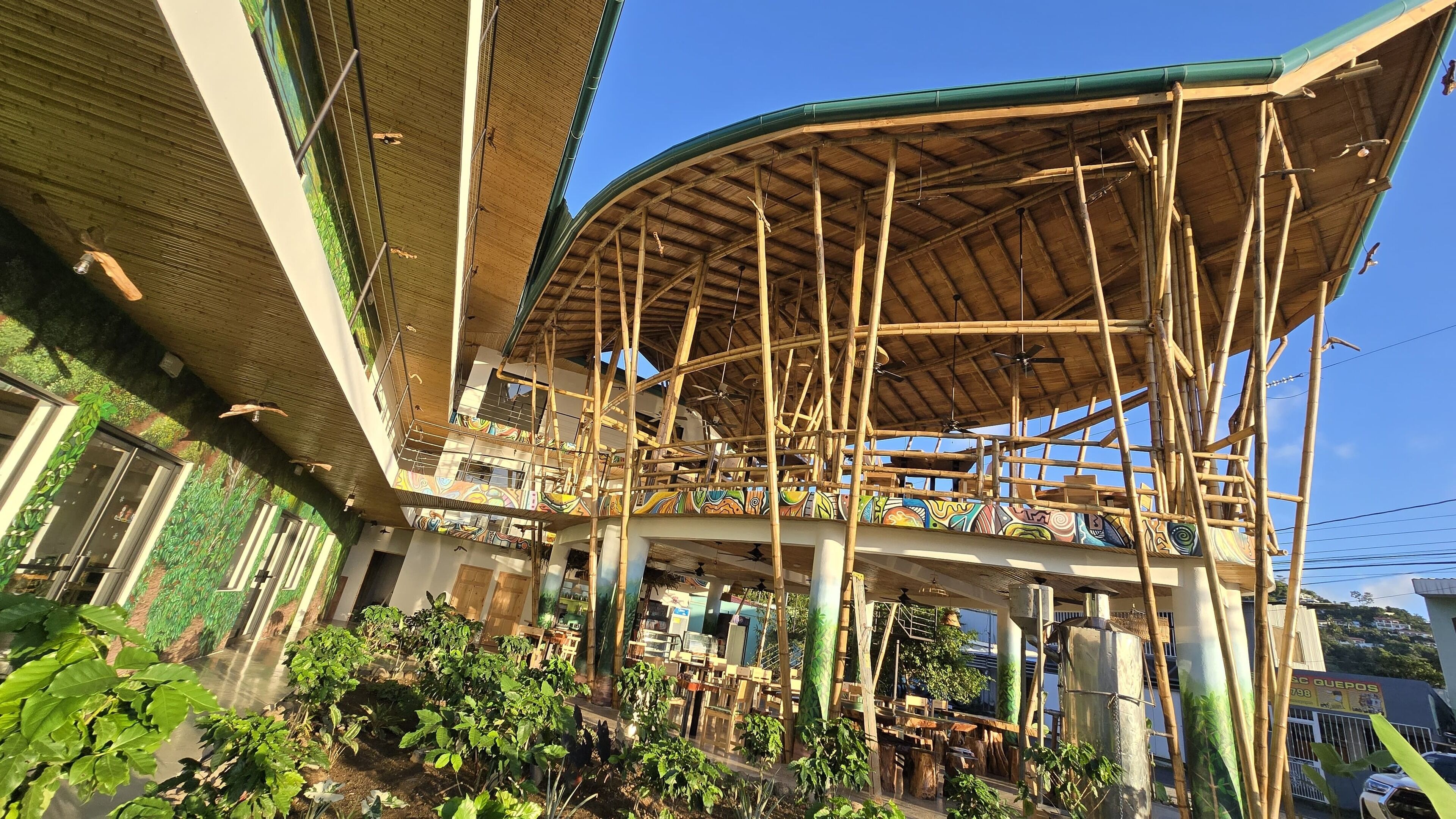 A multi-level structure with bamboo scaffolding, a curved roof, and a view of a street with parked cars.