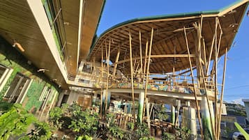 A multi-level structure with bamboo scaffolding, a curved roof, and a view of a street with parked cars.