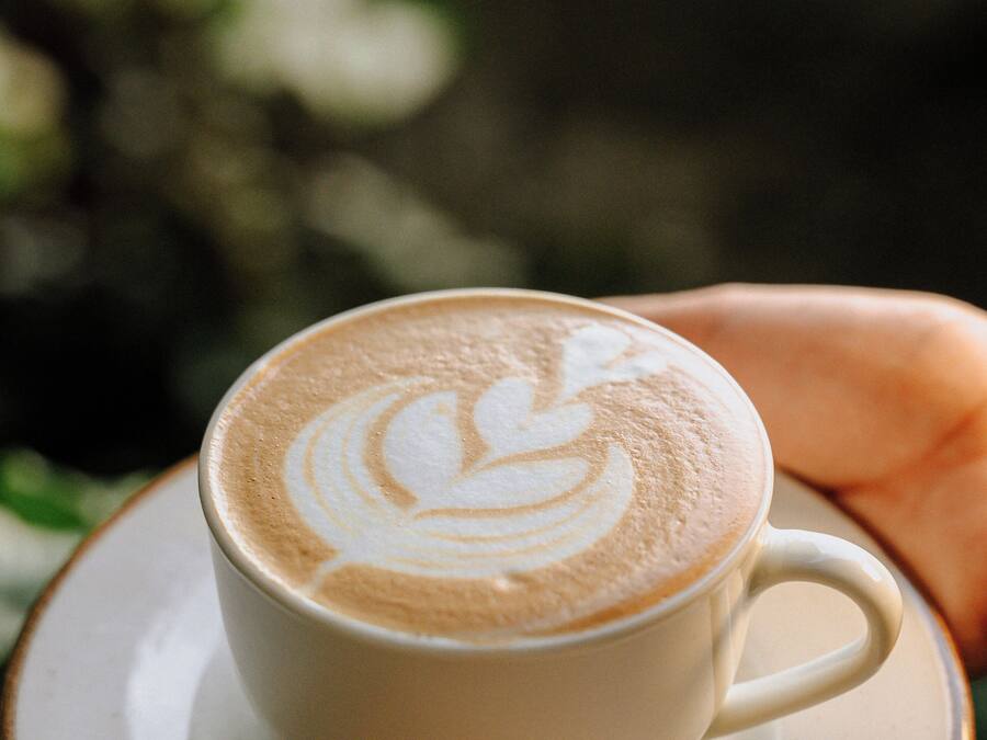 Eine Tasse Kaffee mit Latte-Art auf einem Untertasse, gehalten von einer Hand.