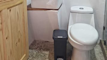 A small bathroom with a wooden door, a white sink with a soap dispenser, a toilet, and a trash bin.