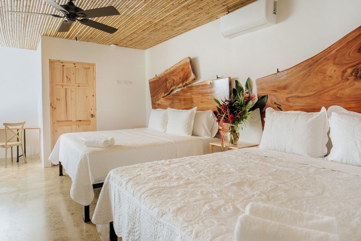 A hotel room with two beds, a wooden headboard, a ceiling fan, and a wooden door.