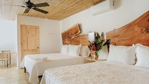 Habitación de hotel con dos camas, cabecera de madera, ventilador de techo y puerta de madera.