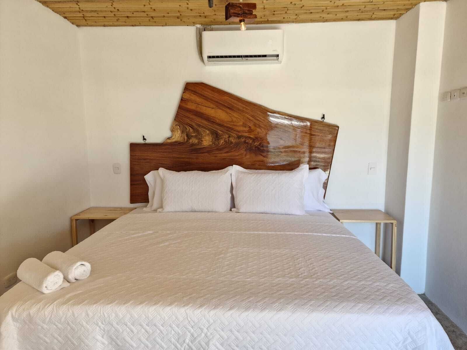 Un dormitorio con una cama grande, cabecera de madera, ropa de cama blanca y dos mesitas de noche.