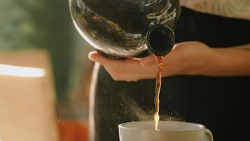 A person pouring coffee from a traditional coffee pot into a cup.