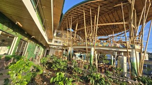 Un edificio de varios niveles con estructura de bambú, plantas al aire libre y un espacio cubierto con mesas y sillas.