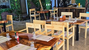 Un restaurante con mesas y sillas de madera, una zona de bar y un techo de bambú.