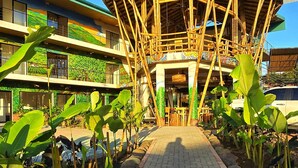 Edificio con estructura de bambú, sendero pavimentado y vegetación circundante.