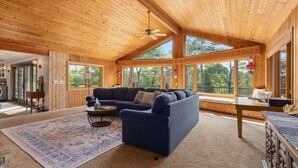 L’intérieur chaleureux d’un chalet avec un canapé bleu, une table à manger en bois et de grandes fenêtres donnant sur le paysage extérieur.