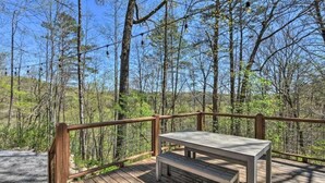 A wooden deck with a table and bench, surrounded by trees.