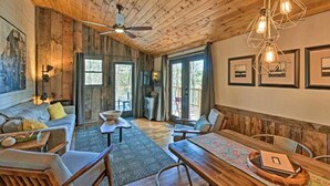 A rustic interior with wooden walls, a ceiling fan, a dining table with chairs, and framed pictures on the walls.