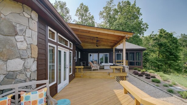 A covered deck with a stone wall, wooden bench, and outdoor seating area.
