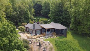 A large, two-story house with a wrap-around porch, surrounded by dense forest.