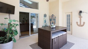 A room with a ceiling fan, a television, a potted plant, a wicker table with cushions, and a door with a cross decoration. - Indian Creek Vacation Home Close to Disney (Kissimmee)