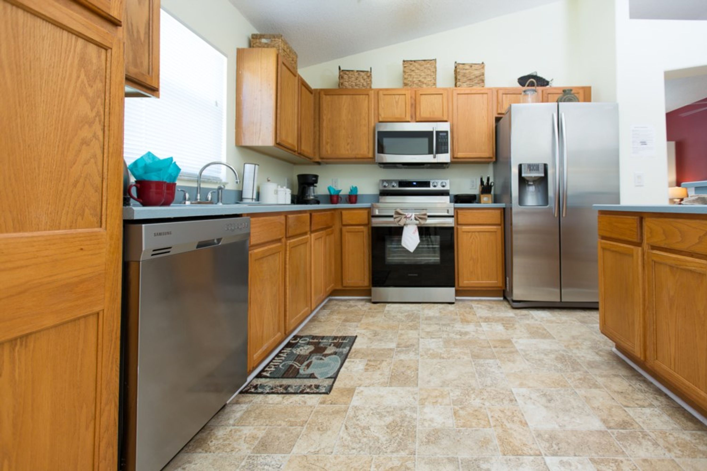 A modern kitchen with wooden cabinets, stainless steel appliances, and a tiled floor.