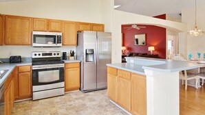 A modern kitchen with wooden cabinets, stainless steel appliances, and a central island. - Indian Creek Vacation Home Close to Disney (Kissimmee)