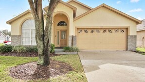 A single-story house with a beige facade, a garage, and a large tree in the front yard. - Indian Creek Vacation Home Close to Disney (Kissimmee)