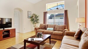 A spacious living room with a large flat-screen TV, a brown leather sofa, a wooden coffee table, and a potted plant. - Indian Creek Vacation Home Close to Disney (Kissimmee)