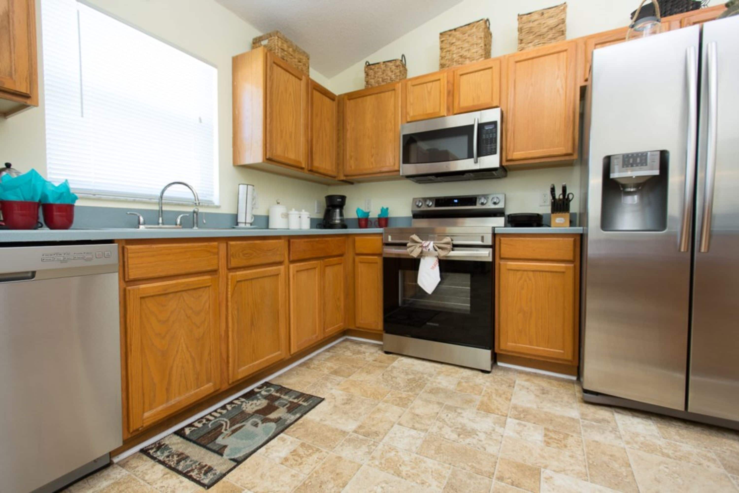 Una cocina con armarios de madera, electrodomésticos de acero inoxidable, microondas, horno y refrigerador.