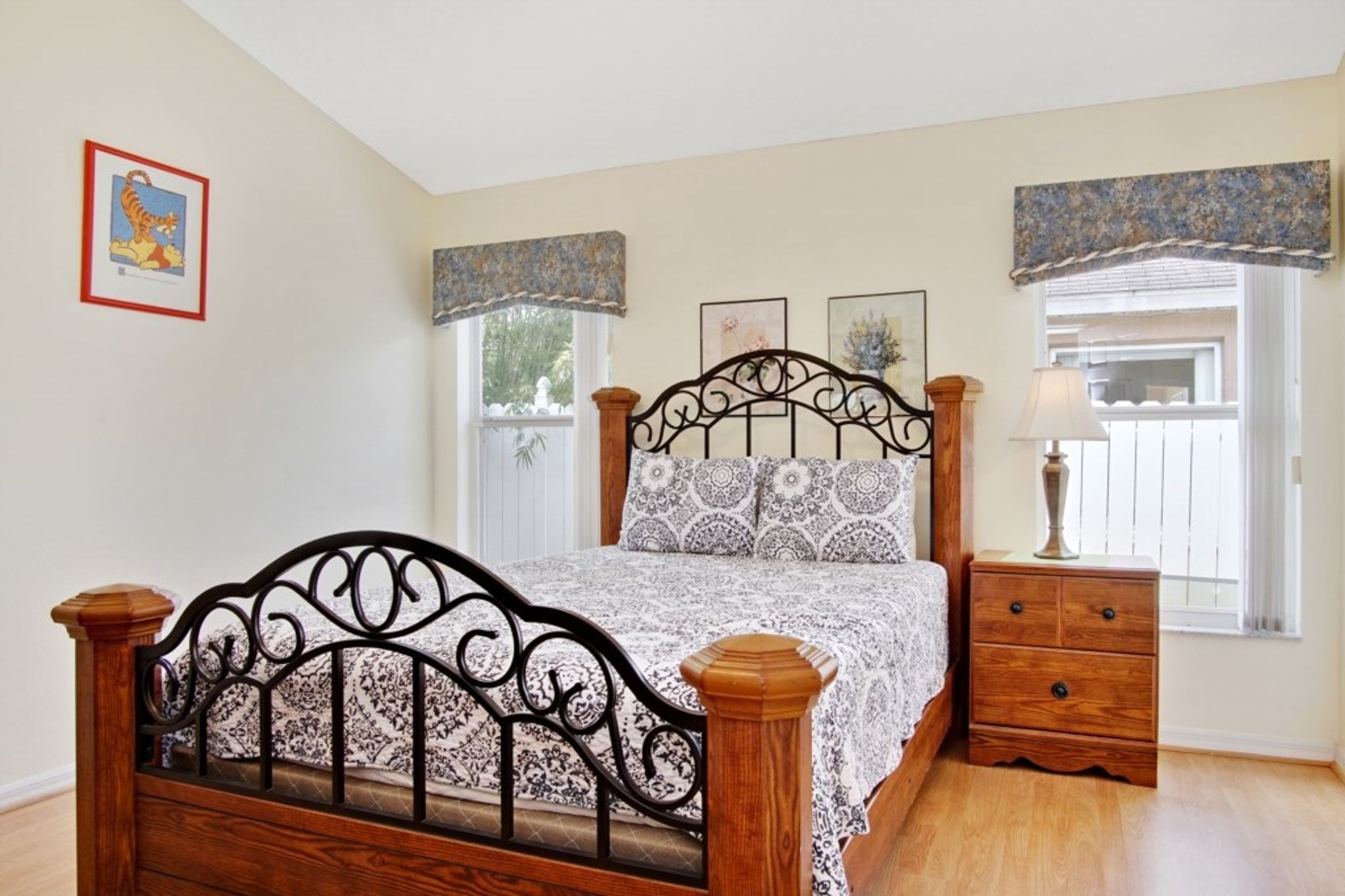 A bedroom with a wooden bed, a nightstand, and two windows with curtains.