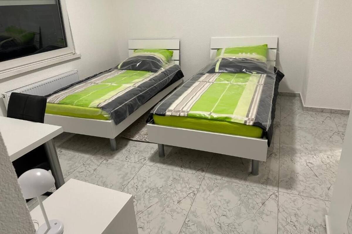 Quarto com duas camas de solteiro, uma escrivaninha e uma cadeira.
