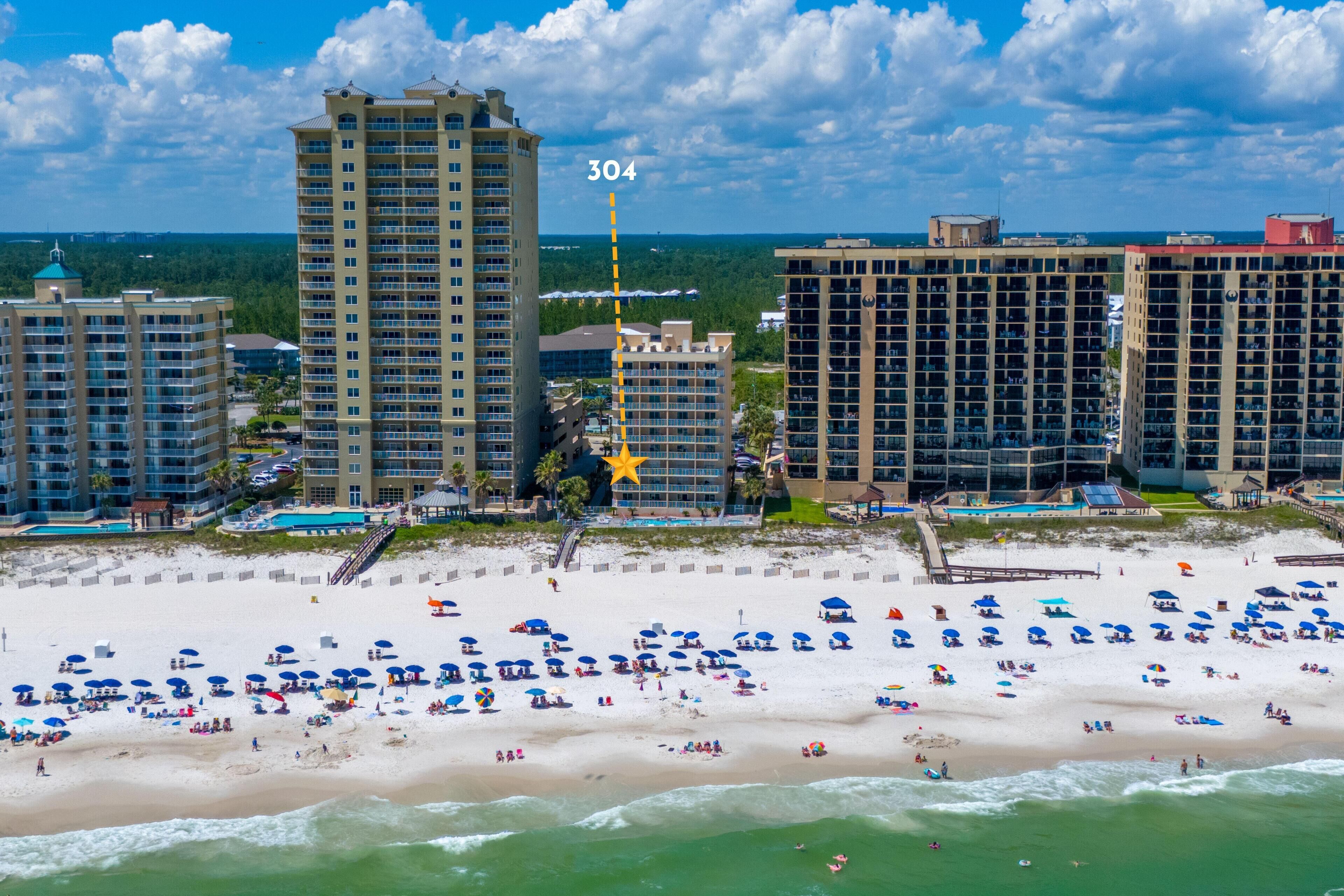 A beachfront hotel with multiple high-rise buildings, a sandy beach with numerous umbrellas, and a clear view of the ocean.