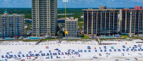 A beachfront hotel with multiple high-rise buildings, a sandy beach with numerous umbrellas, and a clear view of the ocean.