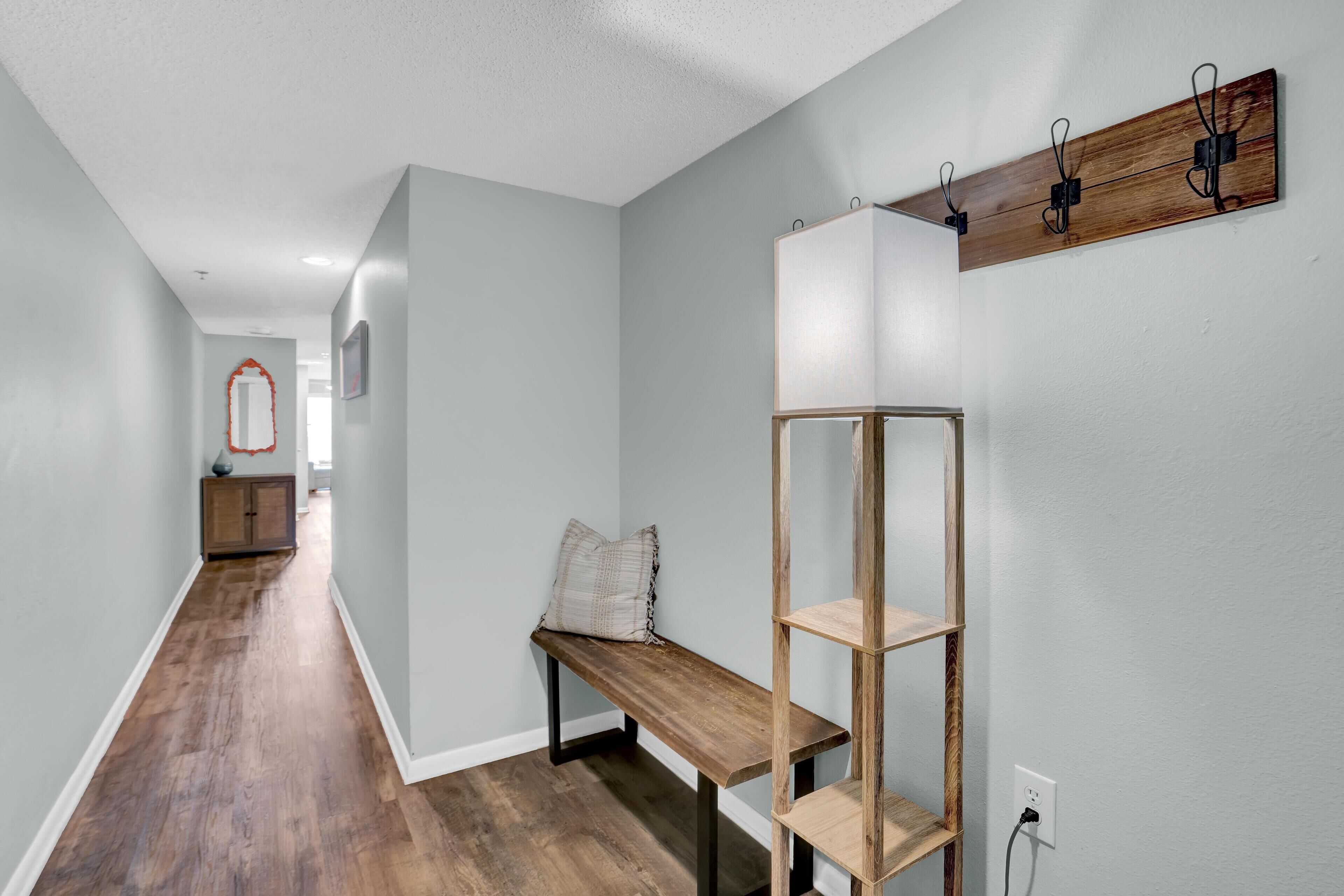 A hallway with a wooden bench, a wall-mounted shelf, and a mirror.