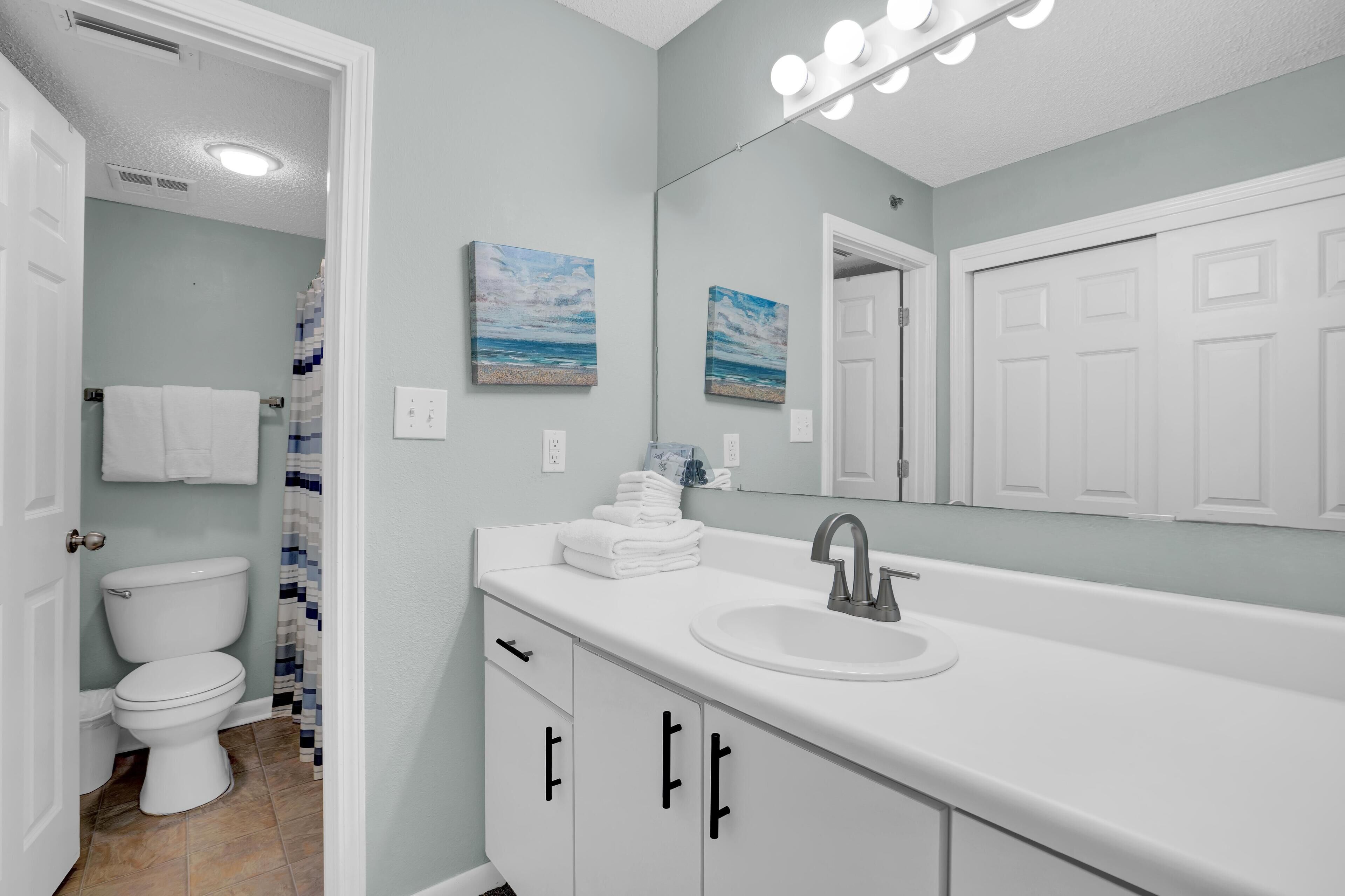 A bathroom with a white sink, a mirror with lights, and a toilet.