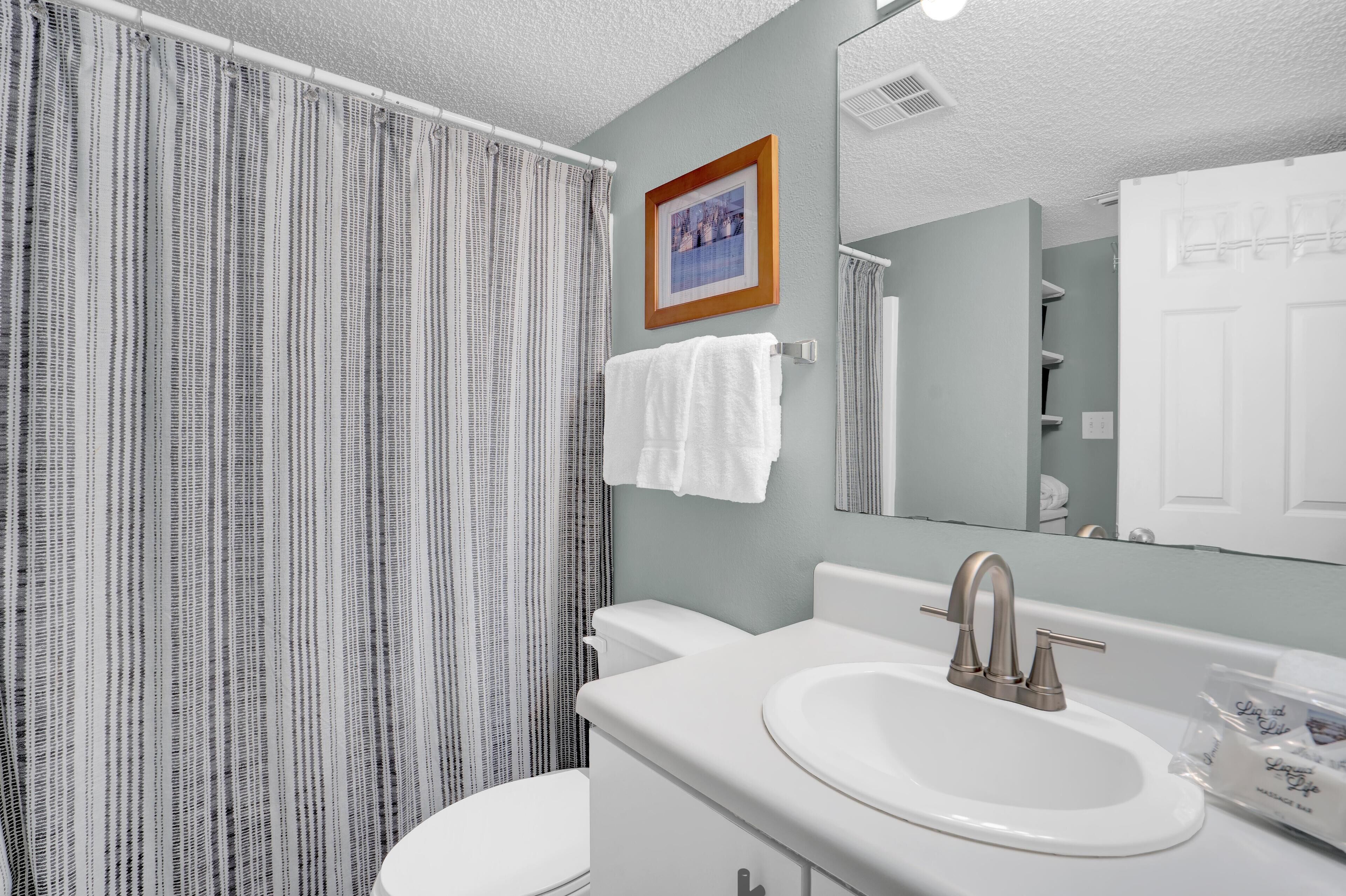 A bathroom with a striped shower curtain, a white sink with a modern faucet, and a framed picture on the wall.