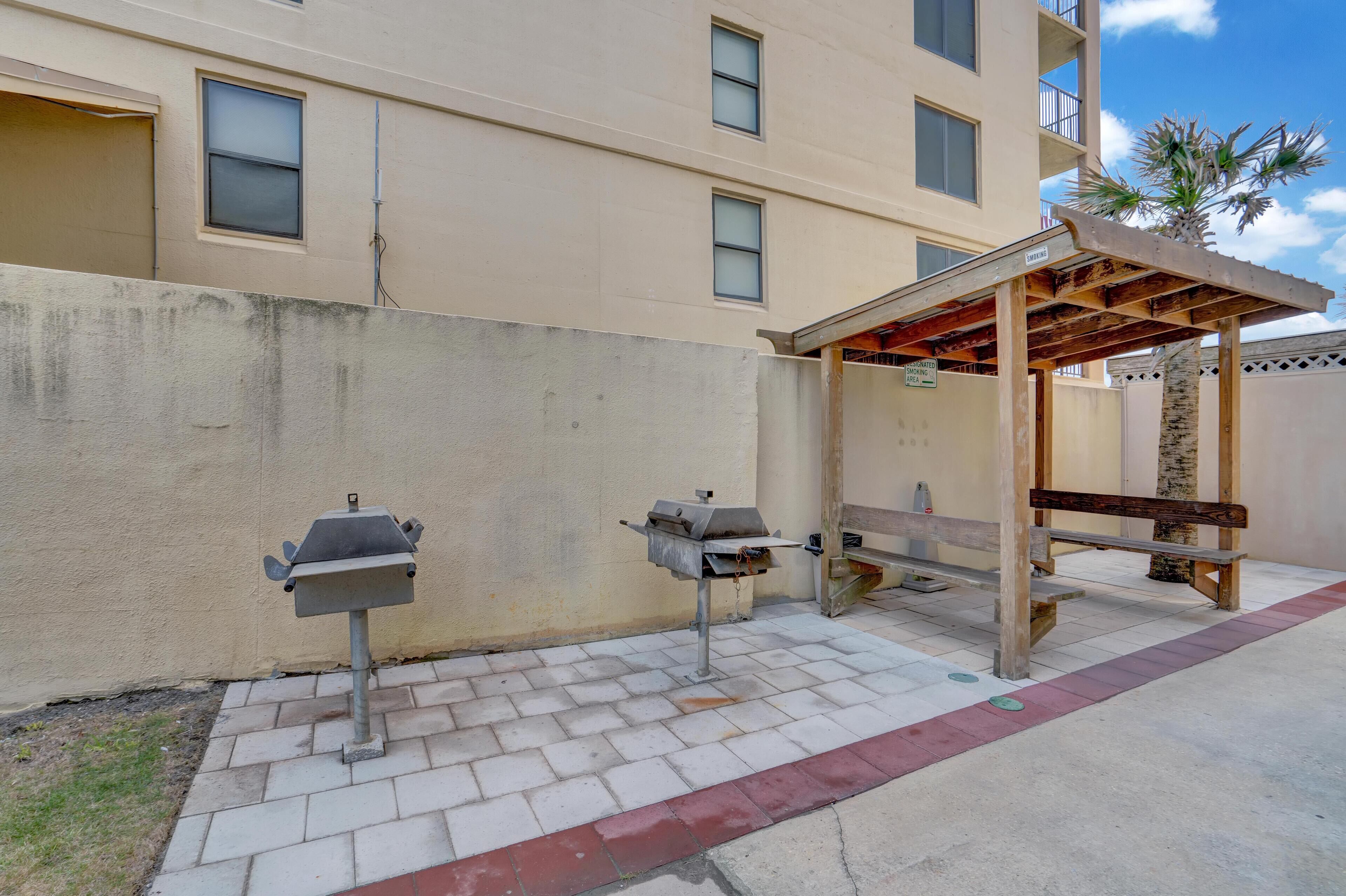 An outdoor patio with a grill, a wooden bench, and a covered seating area.