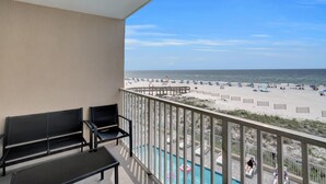 A balcony with two black chairs, a glass table, and a view of a beach with sun loungers and umbrellas. - Four Winds 304 (Orange Beach)