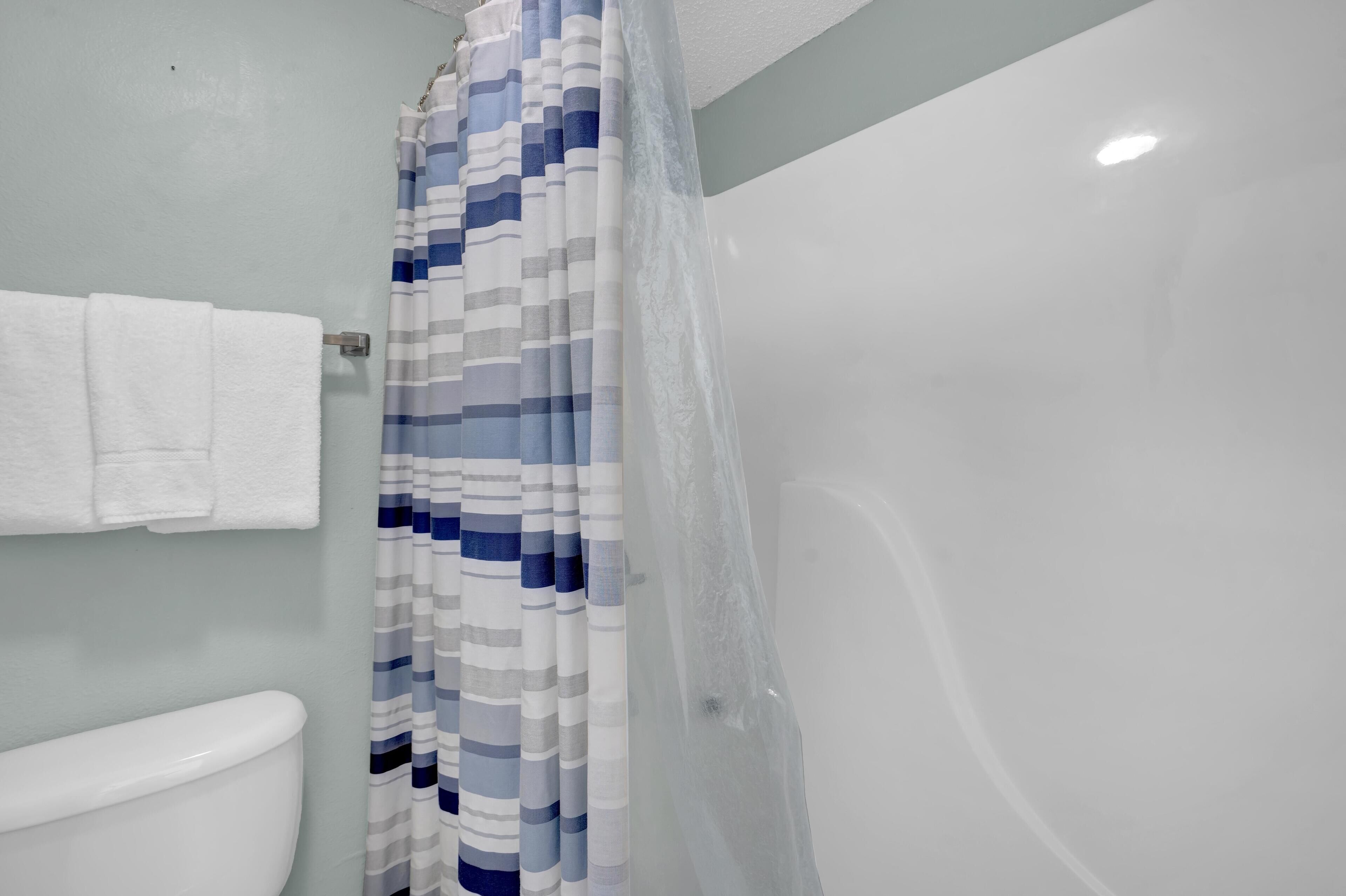 Ein Badezimmer mit Toilette, gestreifter Duschvorhang und Badewanne.